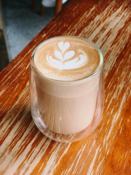 Homemade latte in a ceramic mug with velvety milk foam on a marble countertop, surrounded by coffee beans