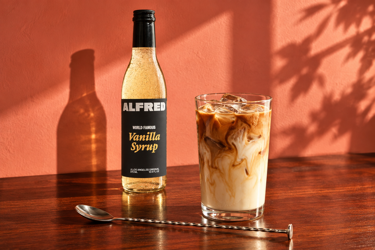 Alfred Vanilla Syrup beside an iced latte on a sunlit coffee bar.