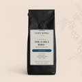 A black coffee bag labeled Cozy Notes The Early Bird+ Breakfast Blend Plus, shown against a warm beige background with subtle coffee bean illustrations on the right.