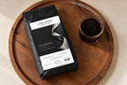 The Signature — coffee bag with approved label beside brewed coffee.