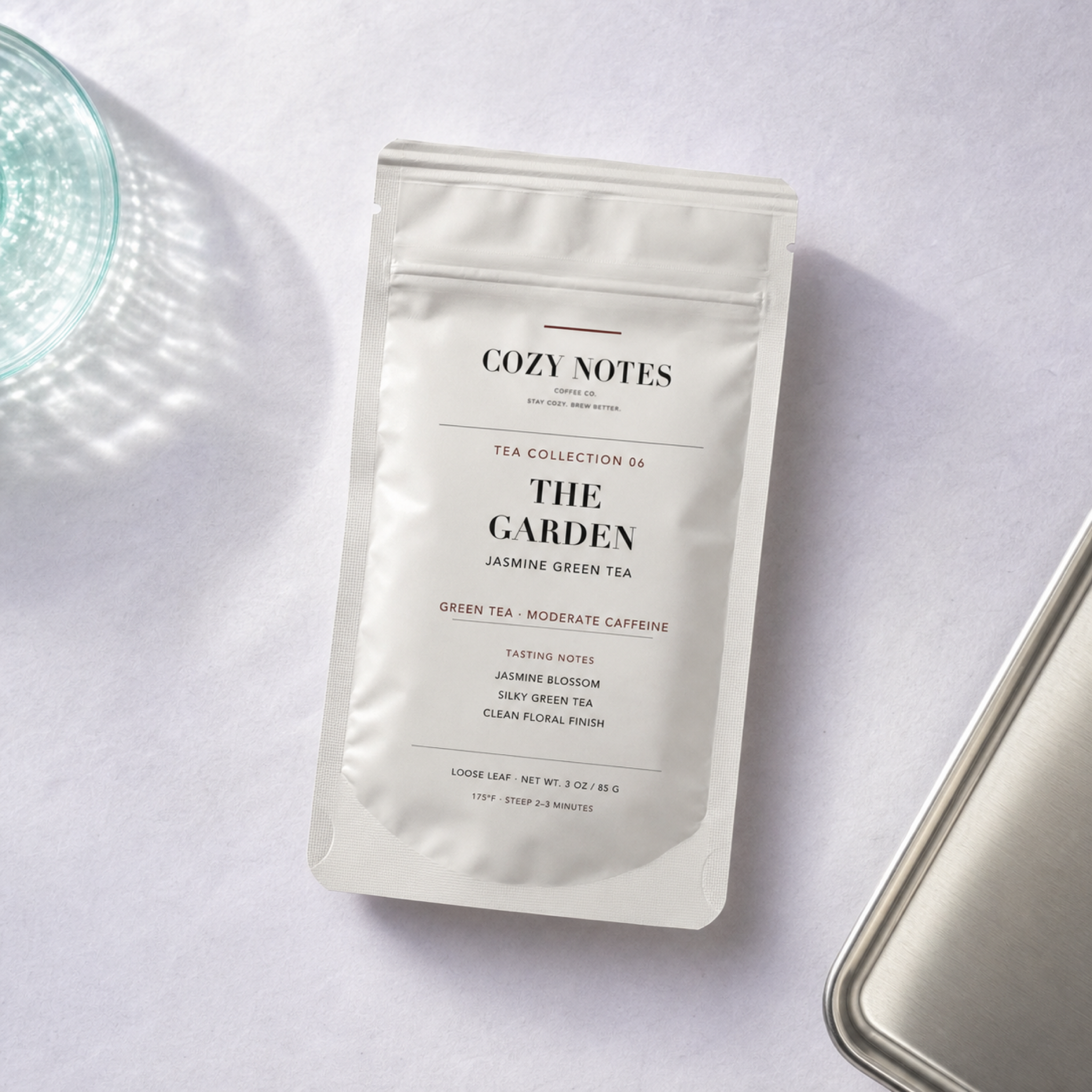 Overhead view of Cozy Notes The Garden jasmine green tea pouch on lilac and silver