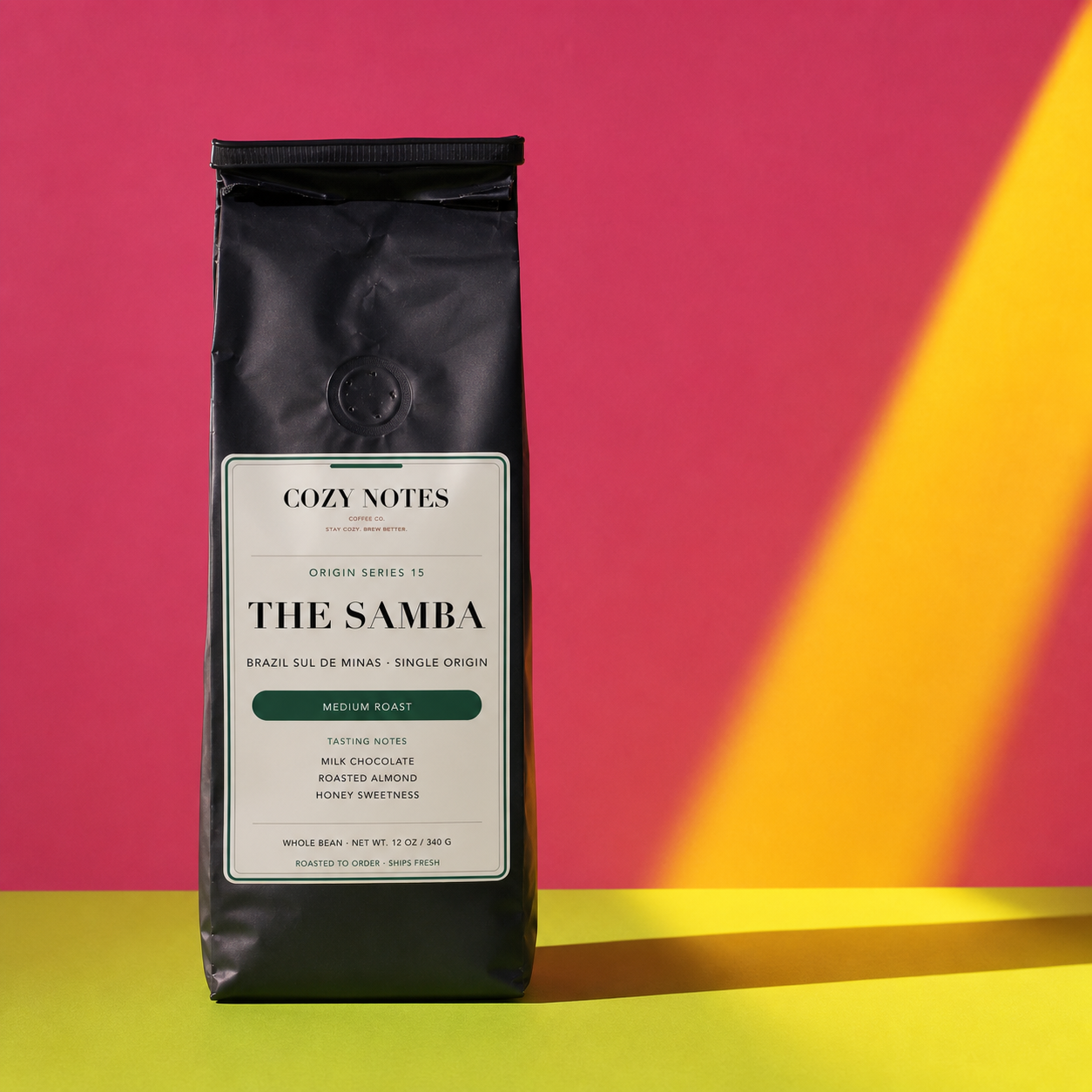 A black bag of Cozy Notes The Samba medium roast coffee stands upright on a bright yellow surface against a pink background with a yellow diagonal light beam.