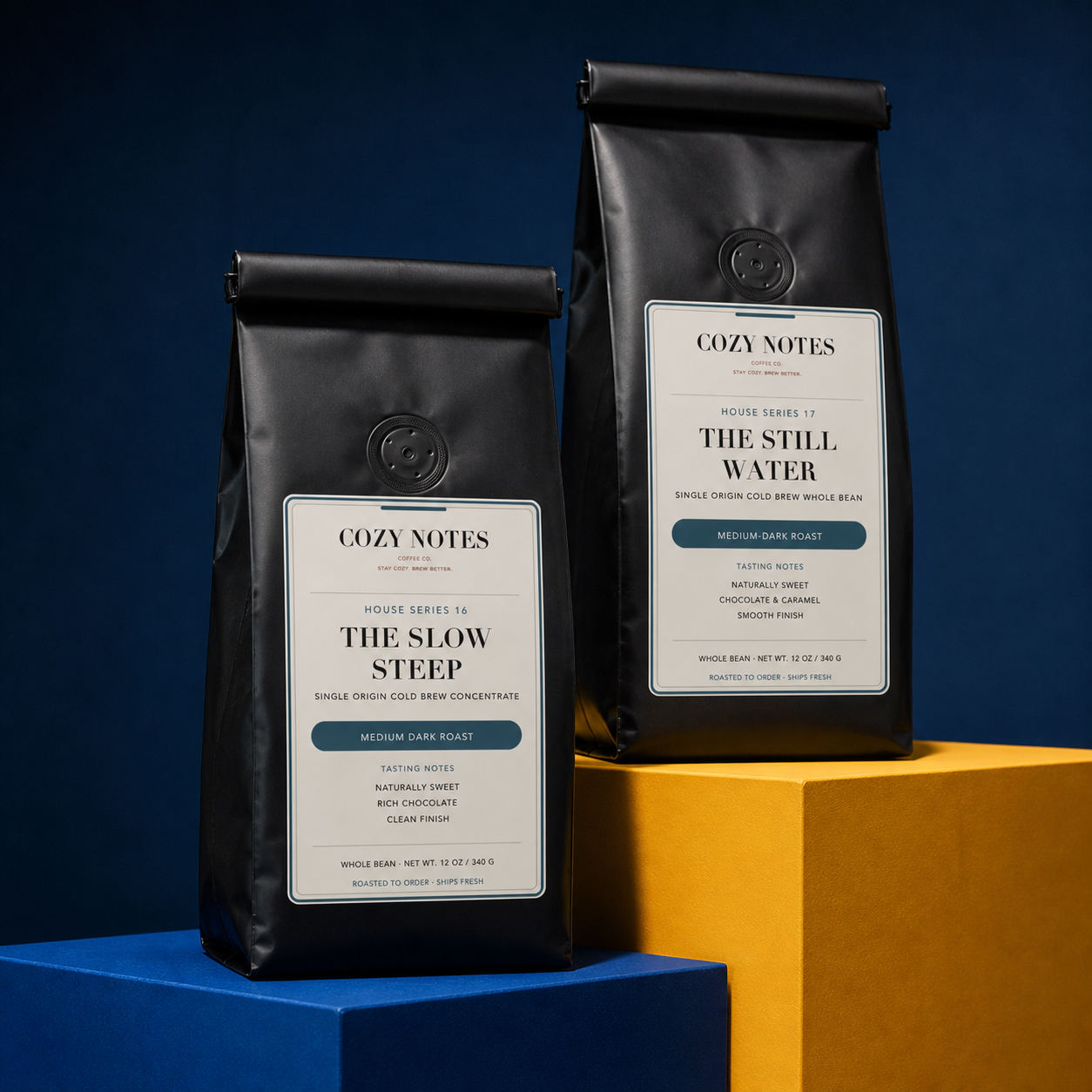 Two black coffee bags from Cozy Notes, labeled 'The Slow Steep' and 'The Still Water', displayed on blue and yellow blocks against a dark blue background.