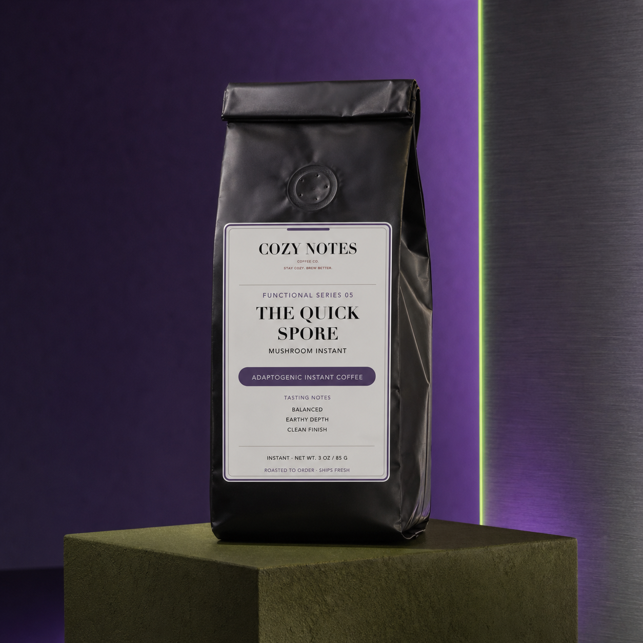A black bag of Cozy Notes The Quick Spore Mushroom Instant coffee stands on a dark green pedestal against a purple and dark gray background with a vertical light strip.