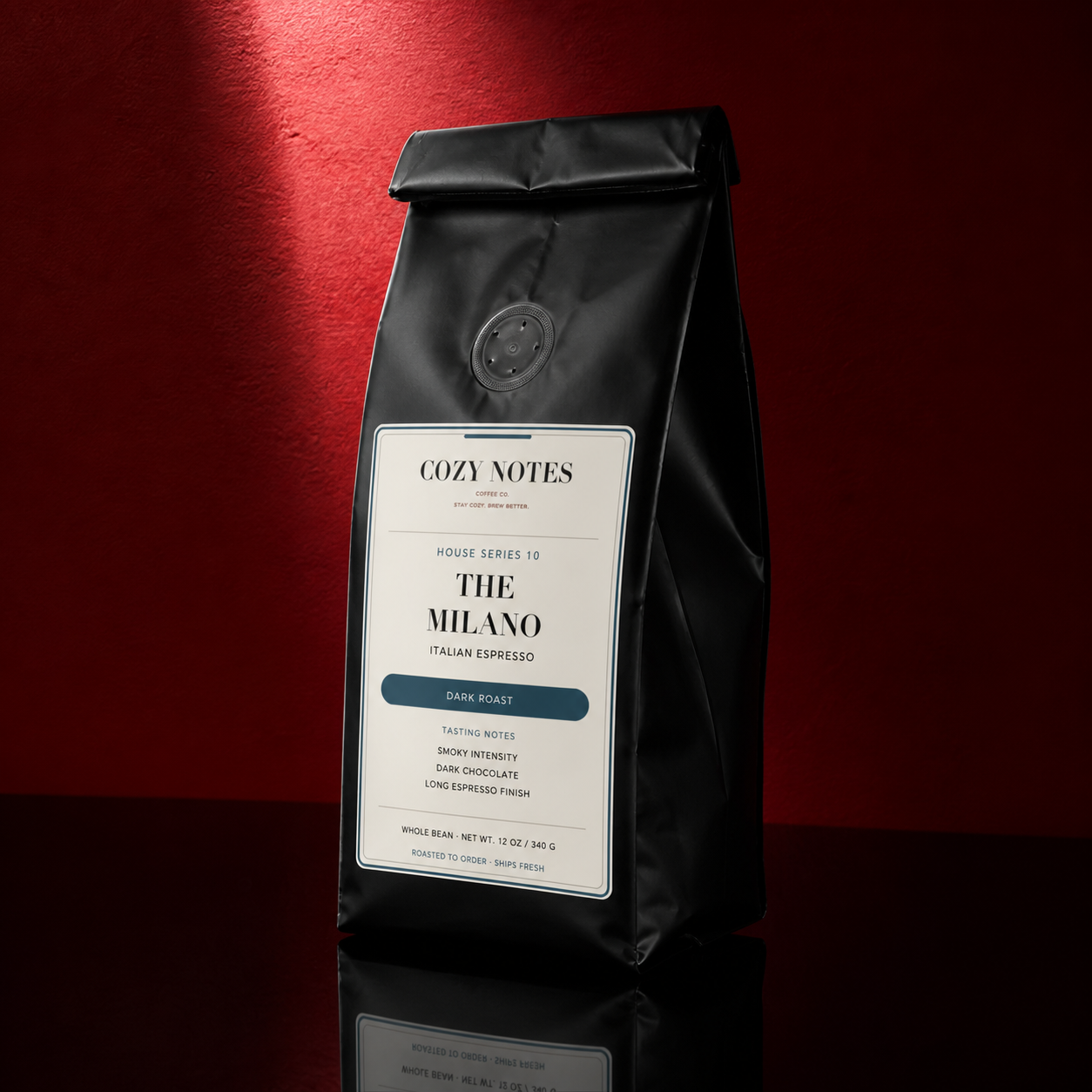 A black coffee bag labeled 'COZY NOTES' and 'THE MILANO' Italian Espresso, standing on a reflective dark surface against a deep red background with dramatic side lighting.
