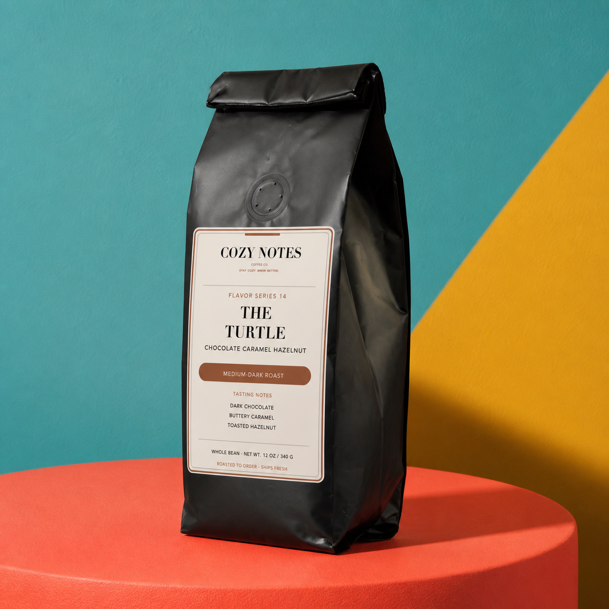 A black coffee bag labeled Cozy Notes The Turtle stands on a red cylindrical pedestal against a split teal and yellow background.