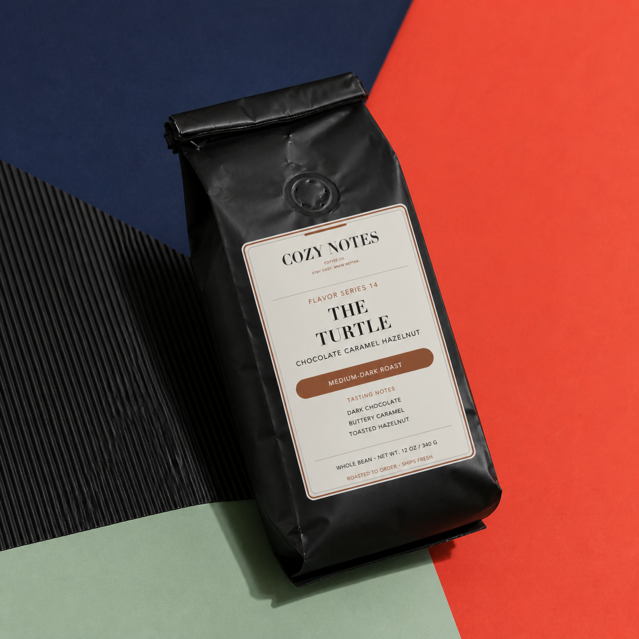 A black bag of Cozy Notes 'The Turtle' medium dark roast coffee beans, styled on a geometric background with navy, red, and light green sections.